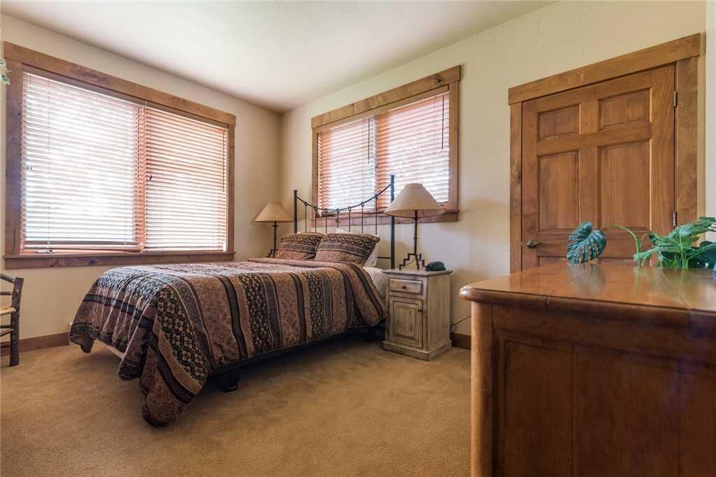 A bedroom with a bed, two bedside tables, a nightstand, a wooden dresser, and a window with blinds.