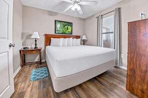 Habitación de hotel con cama, mesita de noche, lámpara, ventilador de techo, ventana con cortinas y armario de madera.