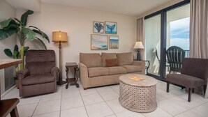 A living room with a sofa, armchairs, a coffee table, and a floor lamp. There are paintings on the wall and a large window with a view. - Perfect Location! Island Winds **Gulf Front One Bedroom** (Gulf Shores)