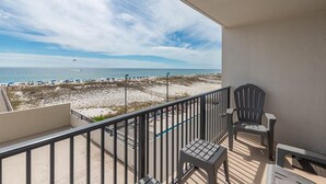 A balcony with a view of the beach, a chair, and a small table. - Perfect Location! Island Winds **Gulf Front One Bedroom** (Gulf Shores)