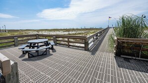 Een houten terras met picknicktafels en een hekwerk met uitzicht op een strand.