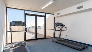 A gym with two treadmills, a large sliding glass door leading to an outdoor area, and a white wall with a vent. - Perfect Location! Island Winds **Gulf Front One Bedroom** (Gulf Shores)