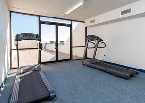 Ein Fitnessraum mit zwei Laufbändern, einer großen Schiebeglastür zu einem Außenbereich und einer weißen Wand mit Lüftung.