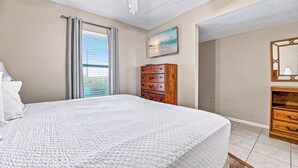 A bedroom with a bed, a dresser, a mirror, and a painting on the wall. - Perfect Location! Island Winds **Gulf Front One Bedroom** (Gulf Shores)