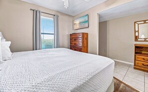 A bedroom with a bed, a dresser, a mirror, and a painting on the wall. - Perfect Location! Island Winds **Gulf Front One Bedroom** (Gulf Shores)