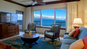 A living room with a television, two armchairs, a sofa, a coffee table, and a view of the ocean.