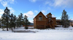 Een houten chalet met garage, omringd door sneeuw en bomen.