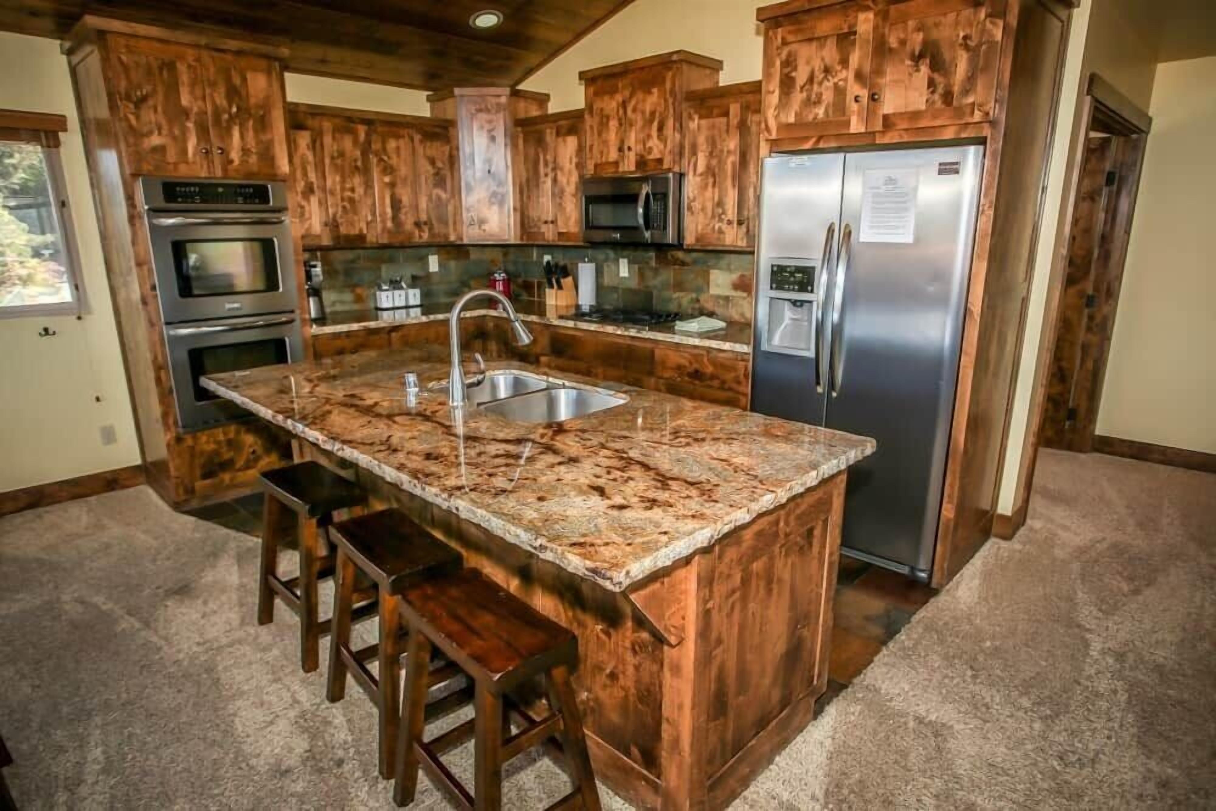 A kitchen with wooden cabinets, a granite countertop, stainless steel appliances, and a built-in island with bar stools.