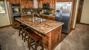 Een keuken met houten kasten, een granieten aanrecht, roestvrijstalen apparatuur en een inbouweiland met barstoelen.