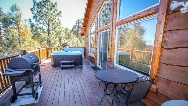 Een houten terras met een hottub, barbecue en tafel met stoelen.