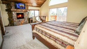 Een slaapkamer met een stenen openhaard, een bed met een geborduurd beddengoed, een aan de muur bevestigde televisie en een balkon met uitzicht.