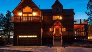 Een houten chalet met twee verdiepingen, een voordeur, een garage en een balkon op de bovenverdieping.
