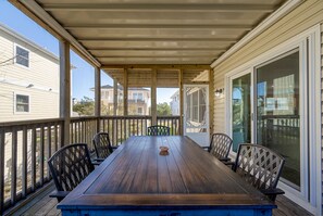 A covered porch with a wooden table and chairs, large sliding glass doors, and a view of neighboring houses.