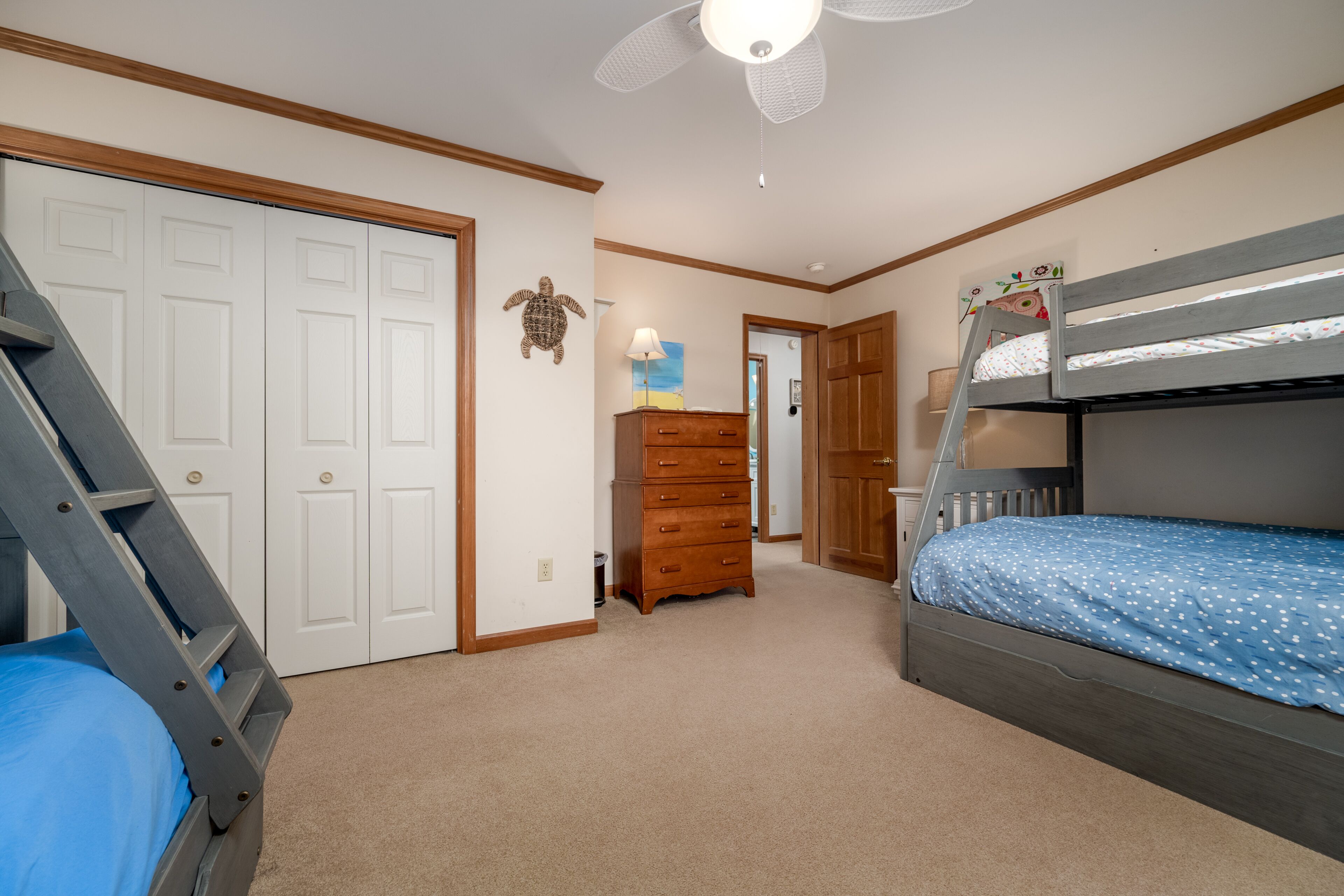 Ein Schlafzimmer mit Etagenbett, Kommode, Lampe und Deckenventilator.
