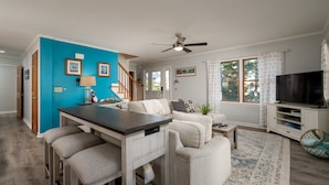 A modern living space with a kitchen area, a dining table with bar stools, a sofa, a TV, and a staircase leading to another level. - Close to the Beach, Pet Friendly/Tesla Charger/2-3 Night Stays Off Season (Milton)