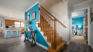A modern kitchen with wooden cabinets, a blue accent wall, and a wooden staircase leading to a bedroom. - Close to the Beach, Pet Friendly/Tesla Charger/2-3 Night Stays Off Season (Milton)
