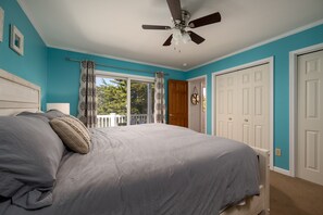 A bedroom with a bed, a ceiling fan, a window with curtains, and a door.