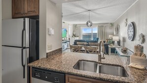A kitchen with granite countertops, stainless steel appliances, wooden cabinets, and a view to the living area. - 🌊 Islander #601 -Gulf Views of the Most Beautiful Beaches in the World! 🏖️ (Destin)