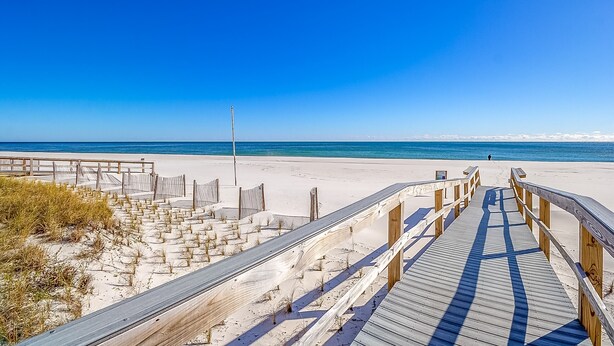Un camí de fusta que condueix a una platja sota un cel blau i clar.