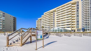 Un hotel a la vora de la platja amb una escala de fusta que condueix a una zona coberta, envoltat d'edificis alts.