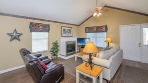 A living room with a fireplace, a ceiling fan, a television, and a door. - Our Tennessee Mountain Home - Great Location!  Close To All The Action! (Pigeon Forge)