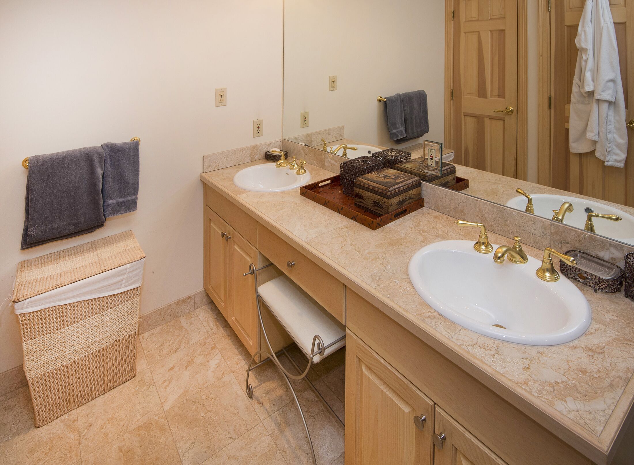 A bathroom with two sinks, a large mirror, wooden cabinets, and a wicker basket.