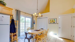 A dining area with a round table, wooden chairs, a chandelier, and a refrigerator. - #119 Sunshine Shores (Pacific City)
