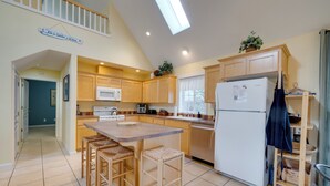 A kitchen with wooden cabinets, a white refrigerator, a dining area with stools, and a staircase leading to an upper level. - #119 Sunshine Shores (Pacific City)