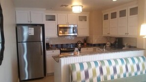 A kitchen with white cabinets, a stainless steel refrigerator, a microwave, and a striped bench. - MARRIOTT OCEAN WATCH (Myrtle Beach)