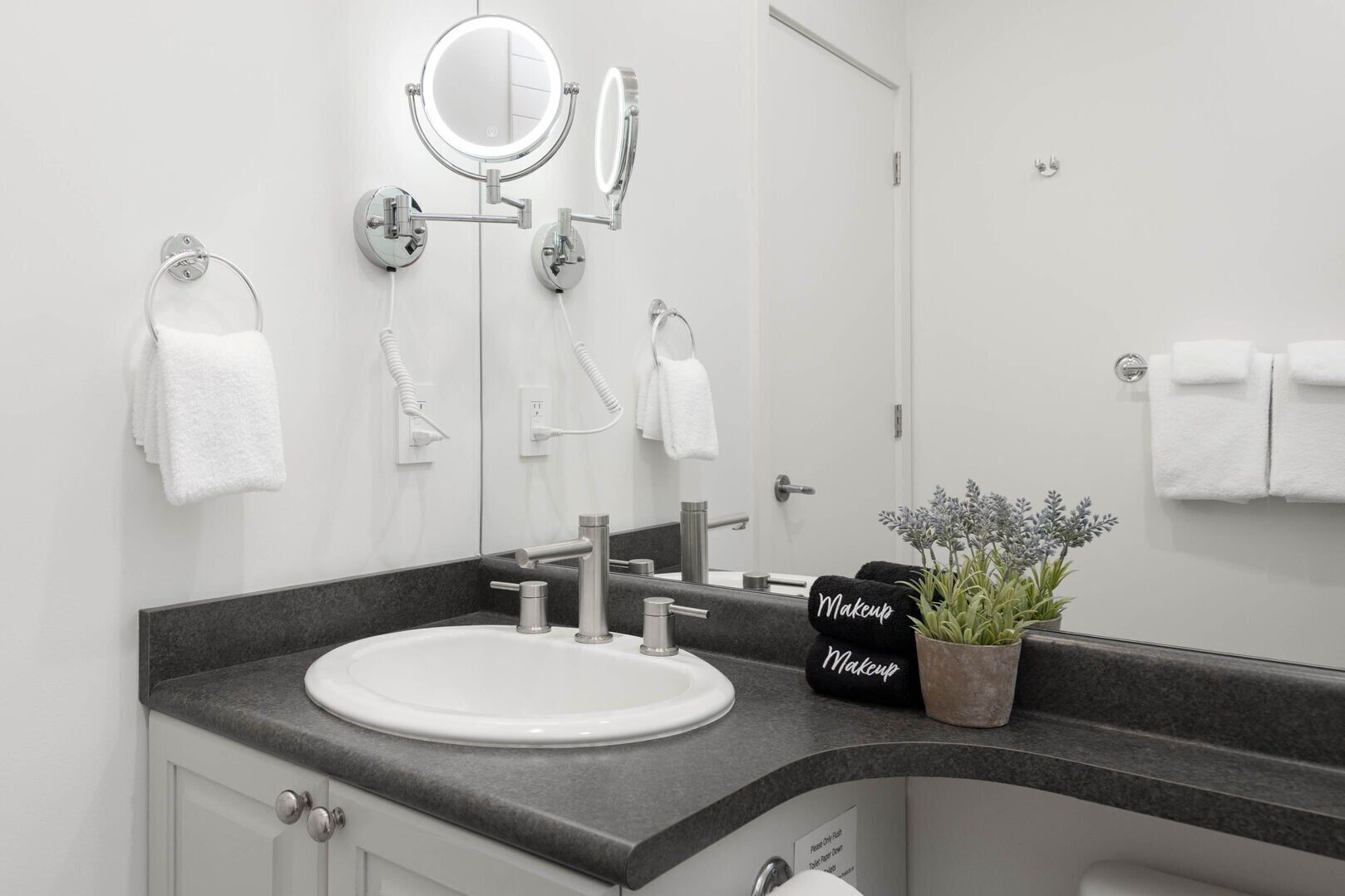 Een moderne badkamer met een wit wastafelmeubel, twee spiegels, een handdoekhouder en een kamerplant.