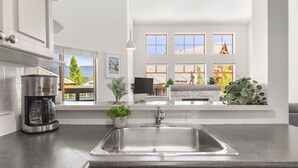 Una cocina moderna con un lavamanos grande, una cafetera y vistas a un paisaje montañoso a través de amplios ventanales.
