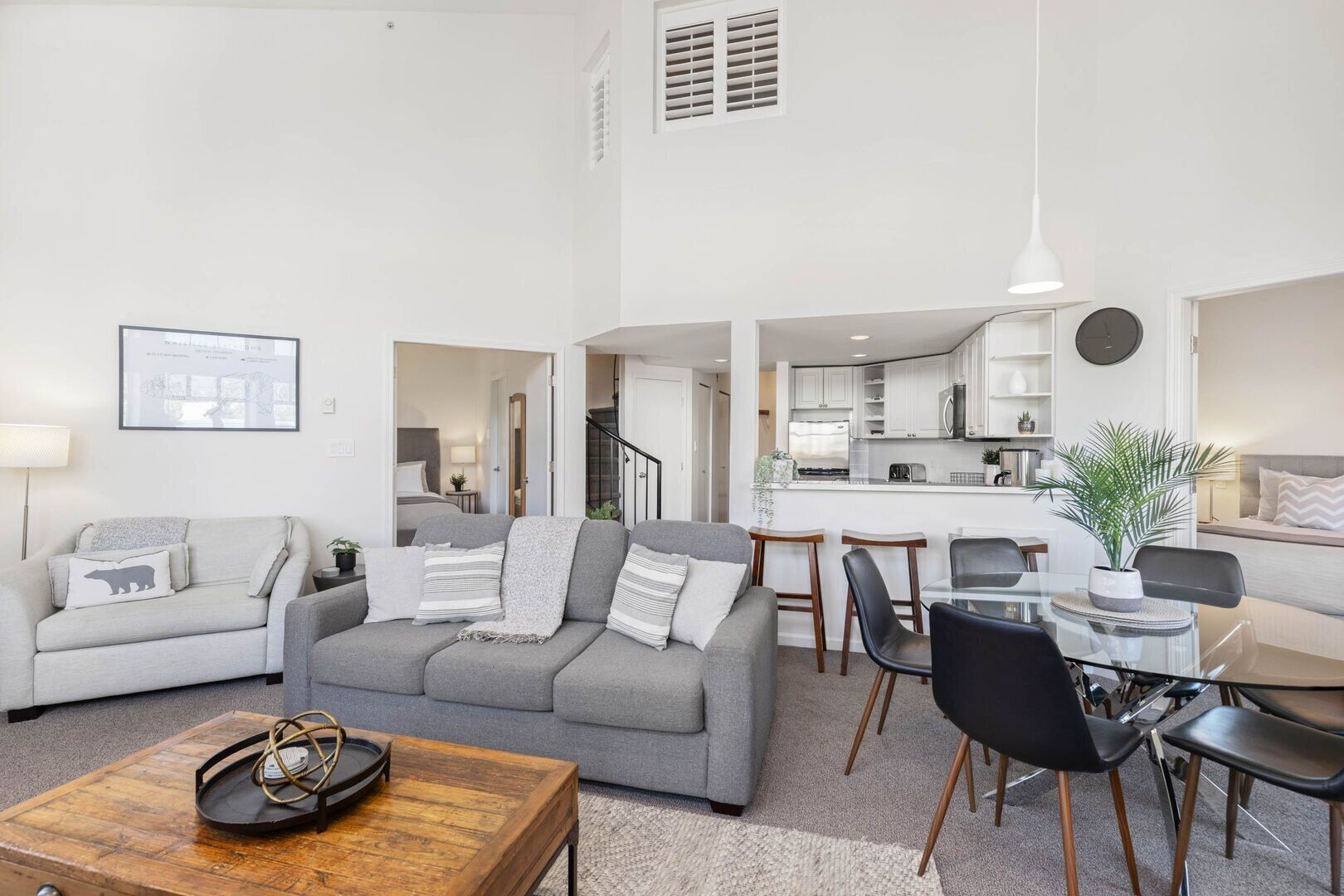 A modern living room with a grey sofa, a coffee table, and a dining area with a glass table and black chairs.
