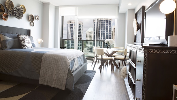 Une chambre moderne avec un grand lit, un coin repas et une vue sur de hauts immeubles.