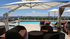 Un espace piscine aménagé sur le toit, avec des meubles en osier, des parasols et une vue sur le panorama urbain.