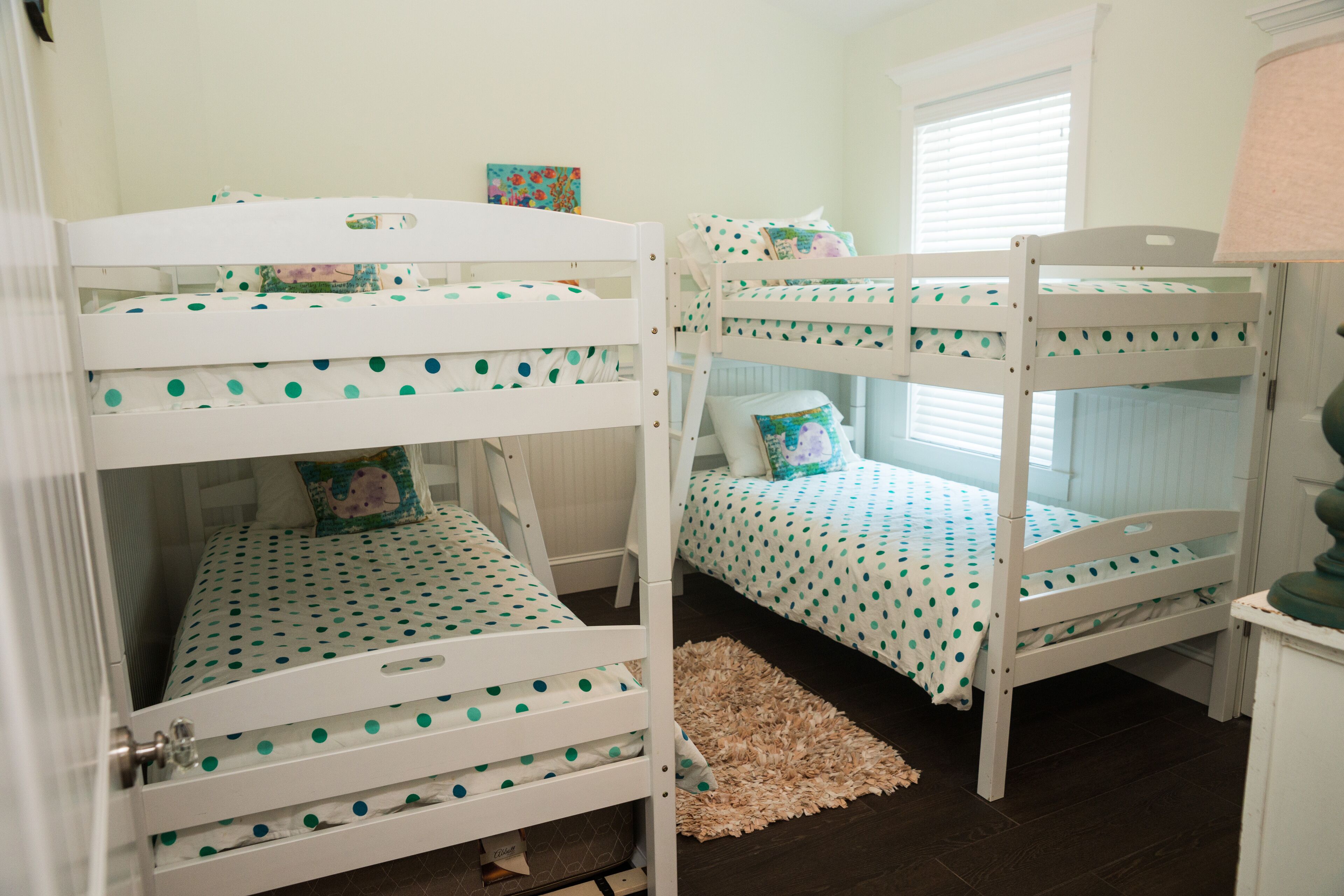 A room with three bunk beds, each with a polka dot bedspread, and a small rug on the floor.