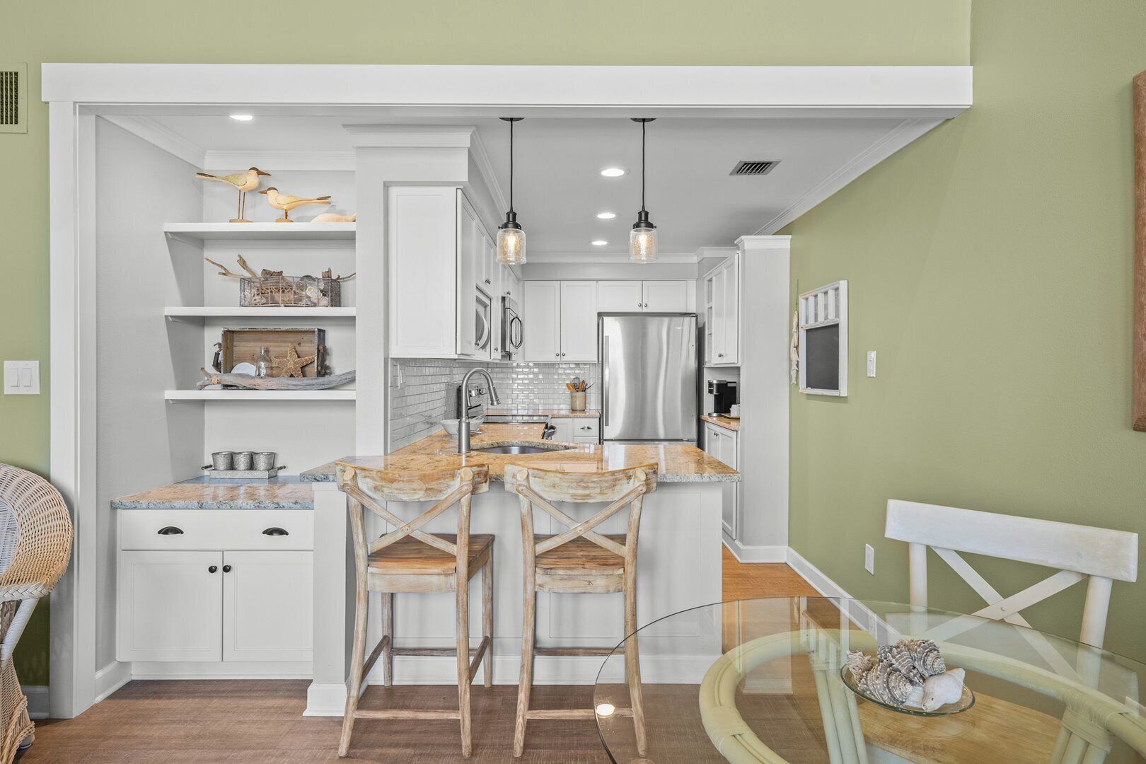 A compact kitchen with white cabinetry, a central island with bar stools, and a hanging light fixture.