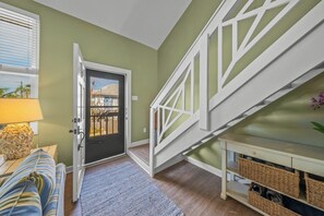 A staircase with white railings leading to a second floor, a door with a view of the outside, a lamp on a side table, and a blue and white striped sofa.