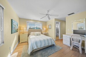 A bedroom with a bed, bedside tables, a desk, a chair, a ceiling fan, and a window.