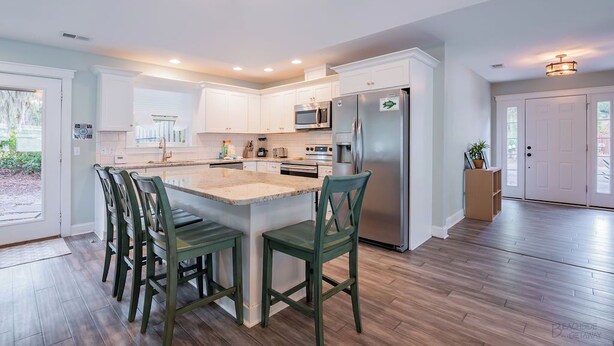 A modern kitchen with white cabinets, a stainless steel refrigerator, and a central island with bar stools. - 13 Sandpiper Street - Pet Friendly (Hilton Head Island)