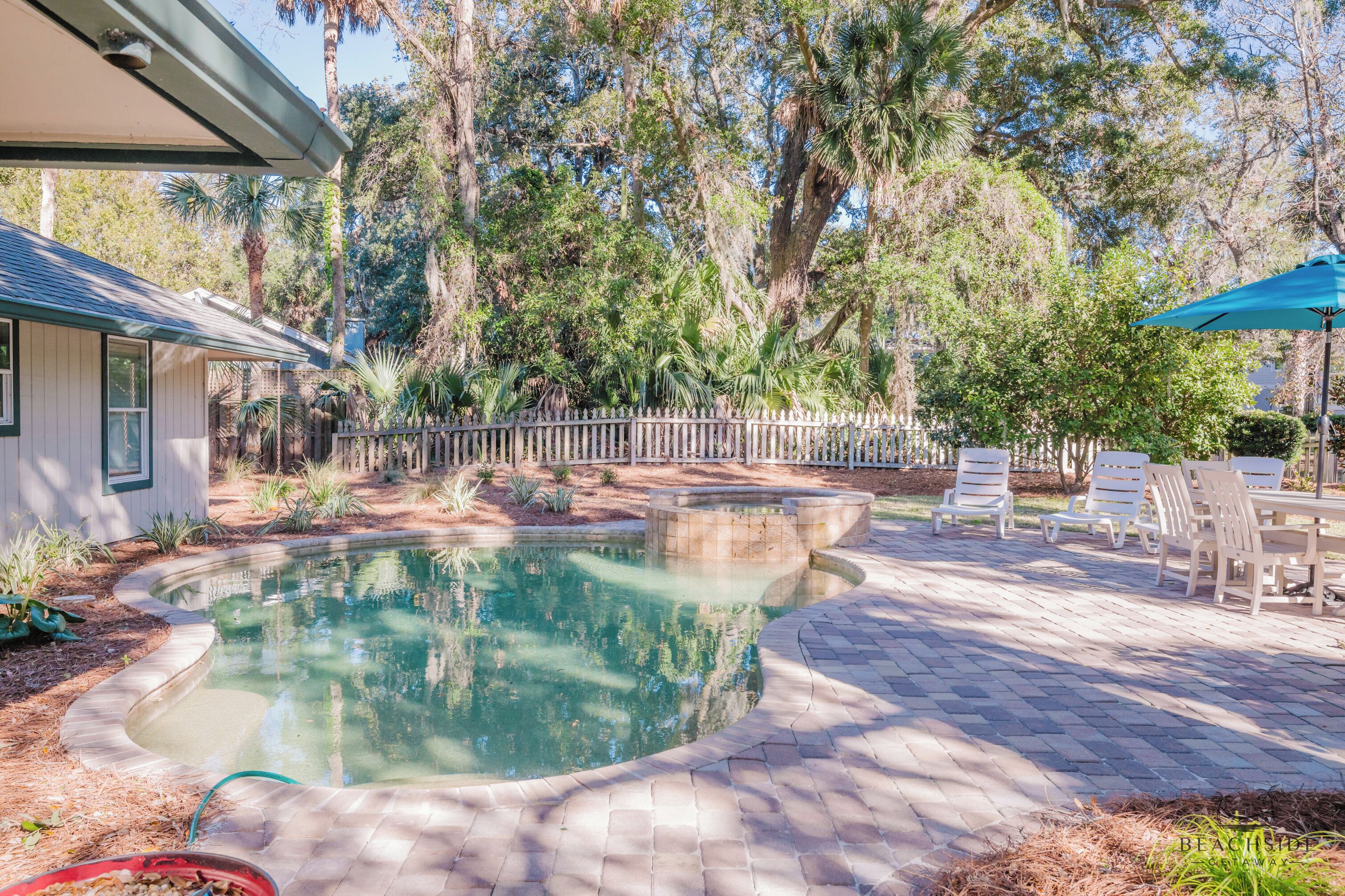 A backyard with a swimming pool, patio furniture, and a wooden fence.