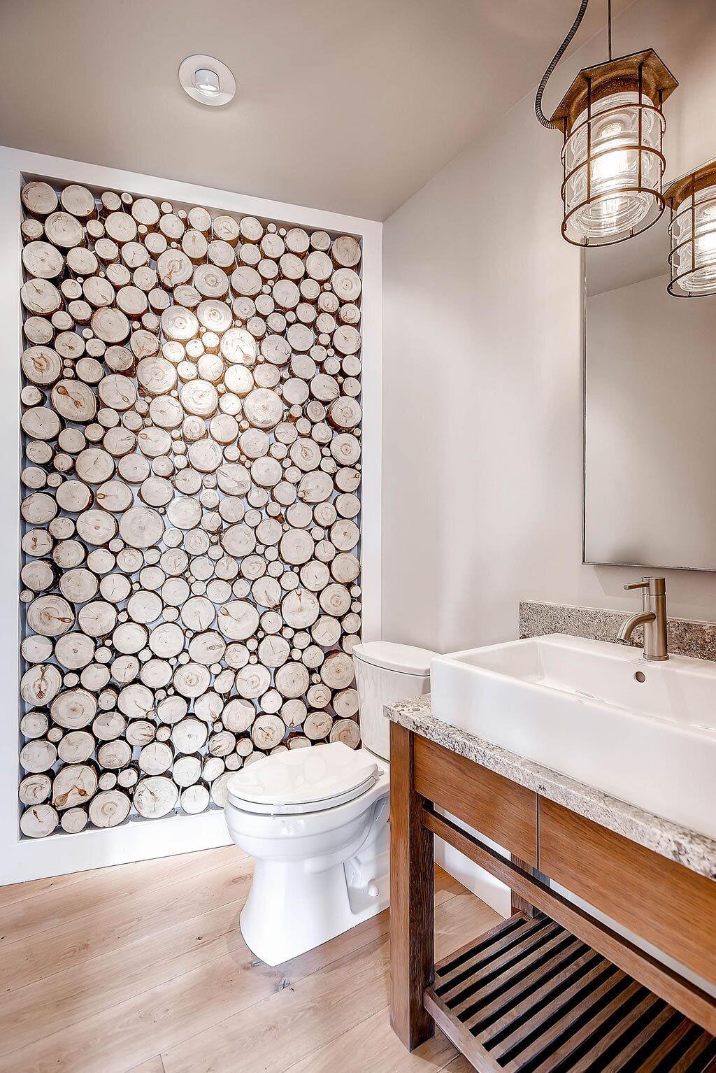 Une salle de bain avec un mur en rondins de bois, des toilettes blanches, un meuble-lavabo en bois et un miroir.