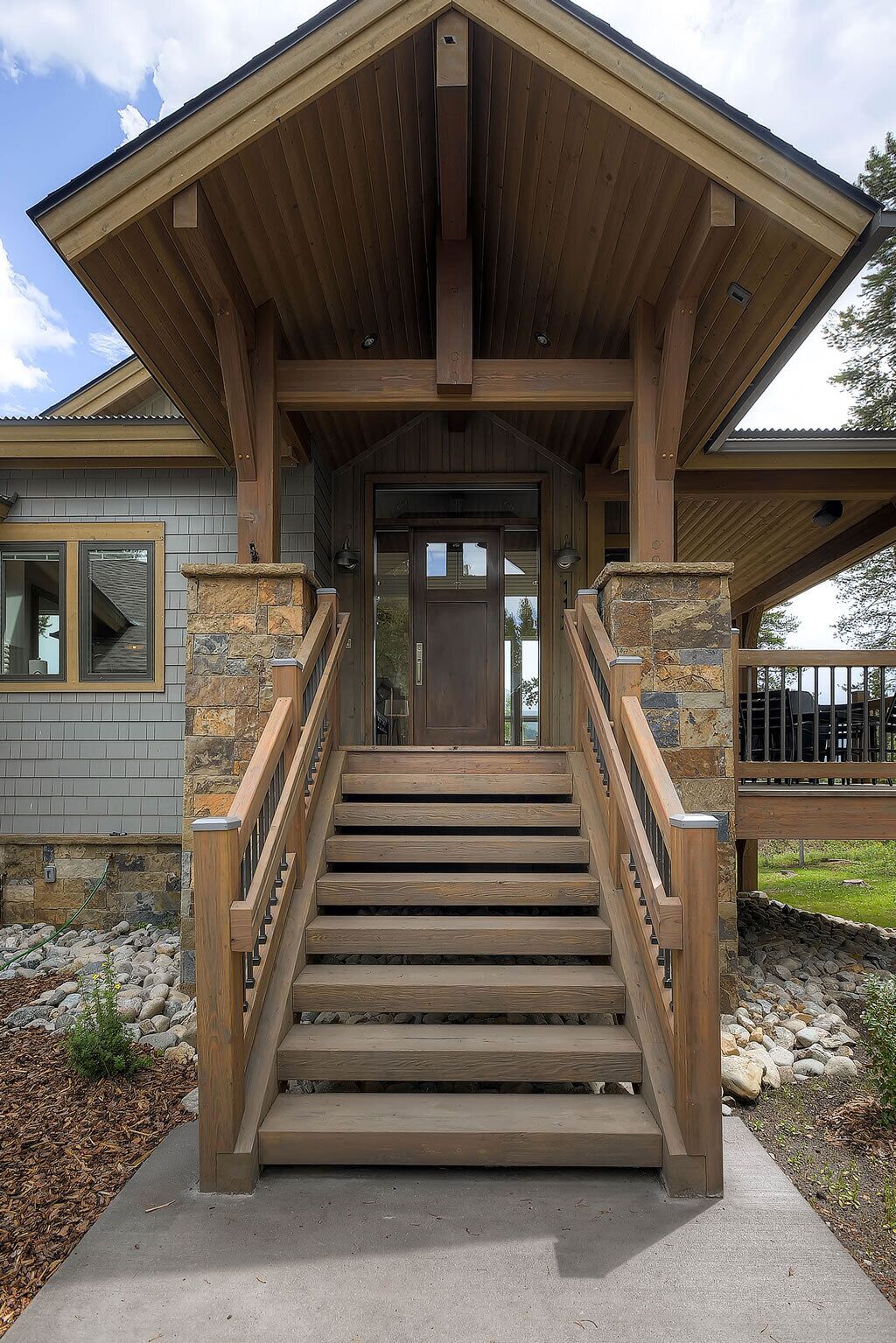 A wooden staircase leading to a house entrance with a stone foundation and a covered porch.
