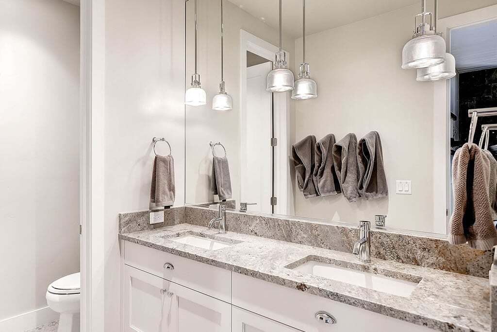 Une salle de bain moderne avec deux vasques, un grand miroir et des luminaires suspendus.
