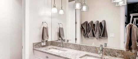 Une salle de bain moderne avec deux vasques, un grand miroir et des luminaires suspendus.