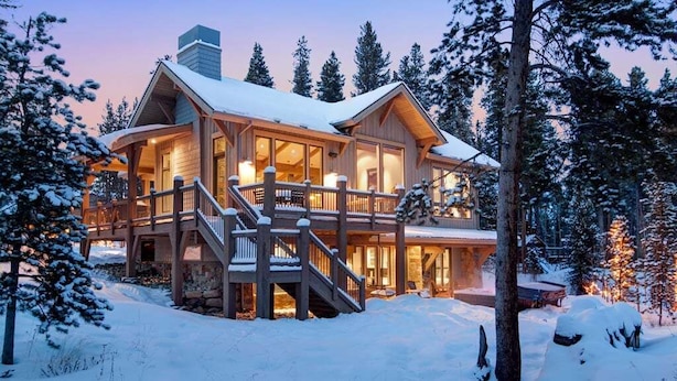 A large, two-story wooden cabin with a covered deck and multiple windows, surrounded by snow-covered trees. - Sunrise Ski Haus: Peak 8 Breckenridge Home with Hot Tub and Views, Near Slopes (Breckenridge)