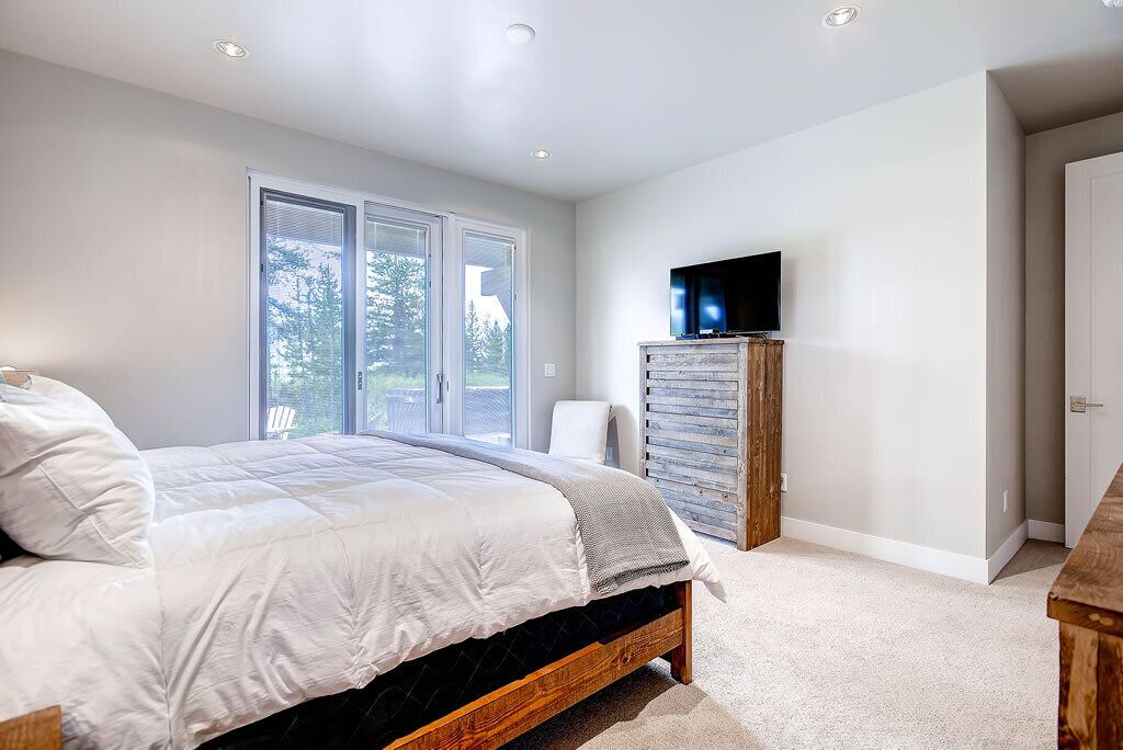 A bedroom with a bed, a television on a wooden cabinet, and a sliding glass door leading to a balcony.