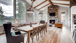 A spacious living room with a large wooden table, comfortable seating, a fireplace, and a television. - Sunrise Ski Haus: Peak 8 Breckenridge Home with Hot Tub and Views, Near Slopes (Breckenridge)
