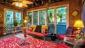 A cozy room with a wooden ceiling, a red sofa, a zebra-patterned rug, and a large window with a view of greenery.