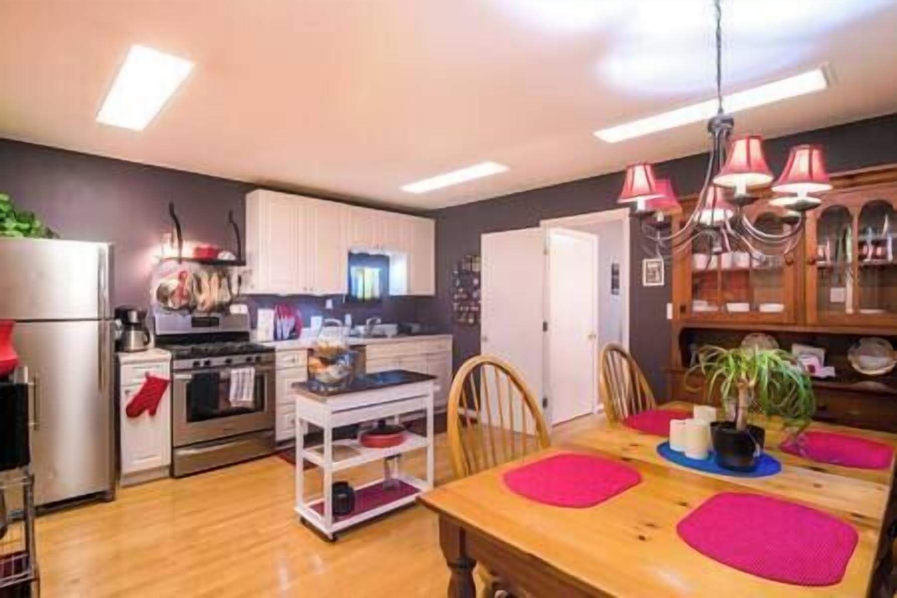A modern kitchen with white cabinets, a wooden dining table with pink placemats, and a chandelier.