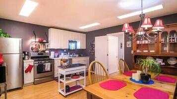 A modern kitchen with white cabinets, a wooden dining table with pink placemats, and a chandelier.
